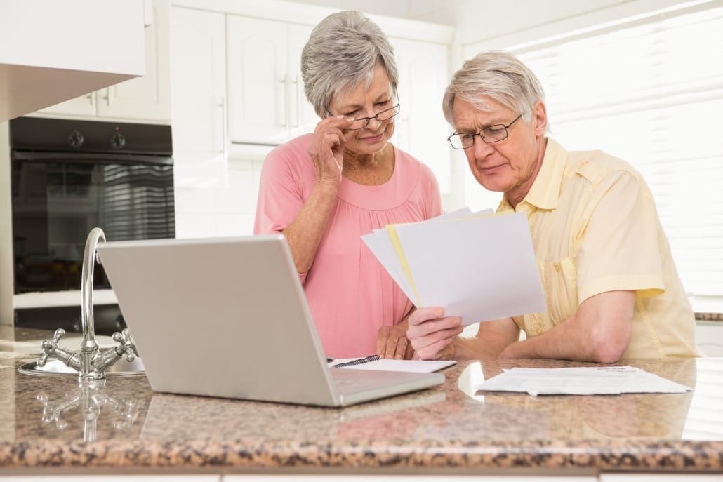 Senior couple paying their bills with laptop at home in the kitchen